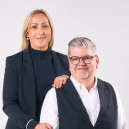 Grit & Frank von Sigiltra Immobilien posieren vor einem hellen Hintergrund